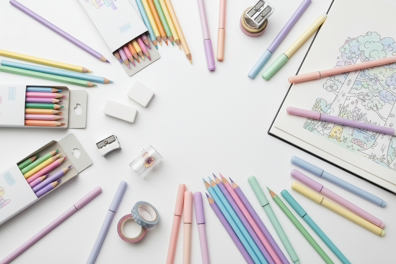 a white desk scattered with pastel coloured pencils and markers and other colouring supplies